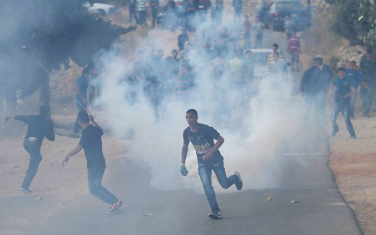 Palestinian protesters throw stones Israeli solider reacts as he runs during clashes