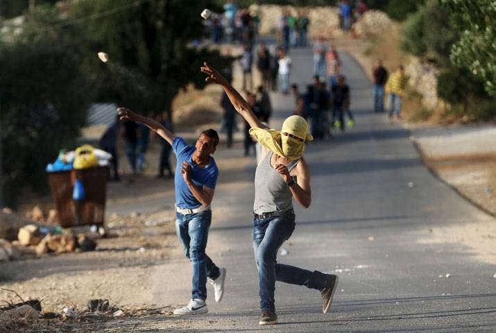 Palestinian protesters throw stones Israeli solider reacts as he runs during clashes