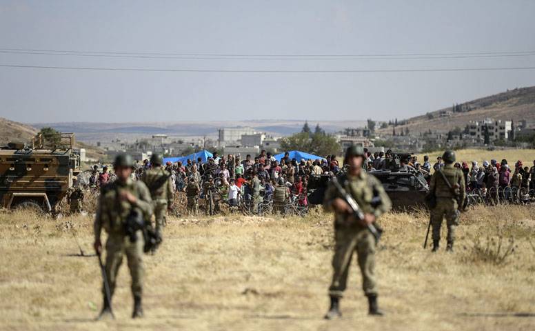 Turkish soldiers stand guard as Kurdish people wait for their relatives who wait near the Syrian border in Suruc
