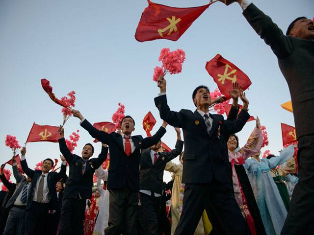 Participants wave flags and flowers during a mass military parade in Pyongyang