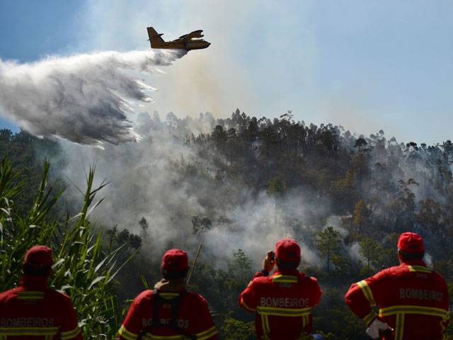 Firefighters watch a helicopter dropping water on a wildfire
