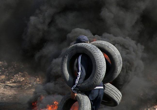 Palestinian demonstrators carries tires to burn clashes with Israeli forces